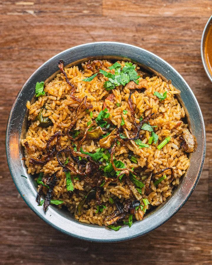 Chicken biriyani in a steel bowl, topped with fried onions and coriander