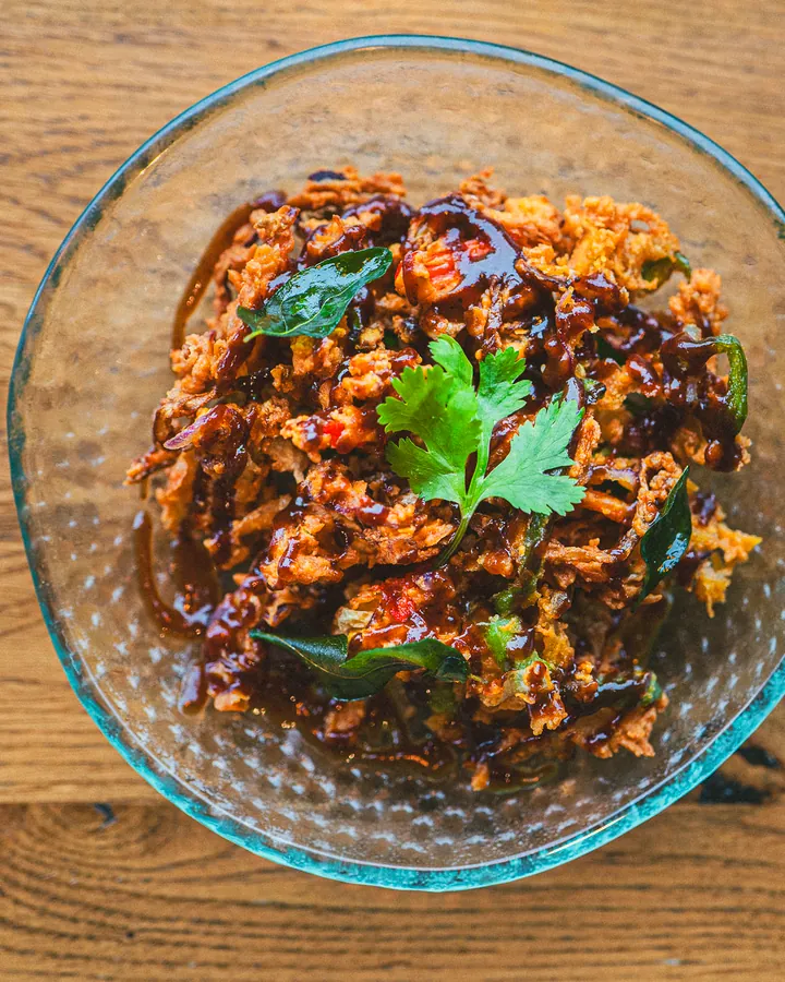 Shredded beef in a dark chilli glaze with curry leaves and coriander, in a glass bowl