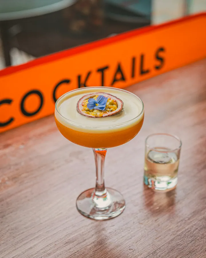 A passion fruit martini with half a passion fruit and a flower on top, and a shot of prosecco beside it