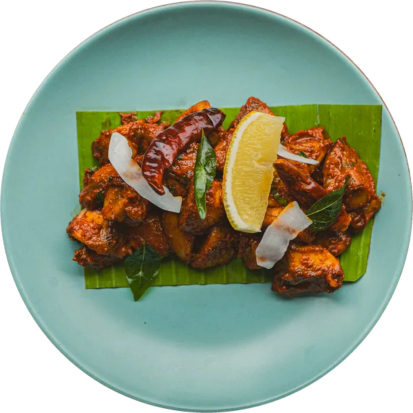 Fried chicken pieces with lemon, coconut and dried chilli, on a piece of banana leaf on a turquoise plate