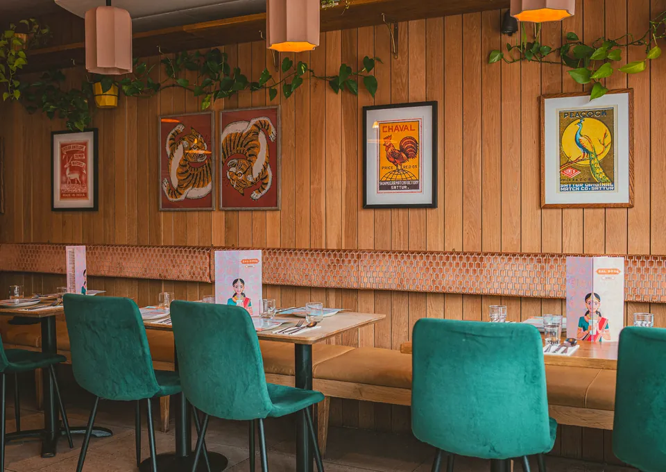 Green velvet chairs along a wood-panelled wall hung with vintage Indian prints