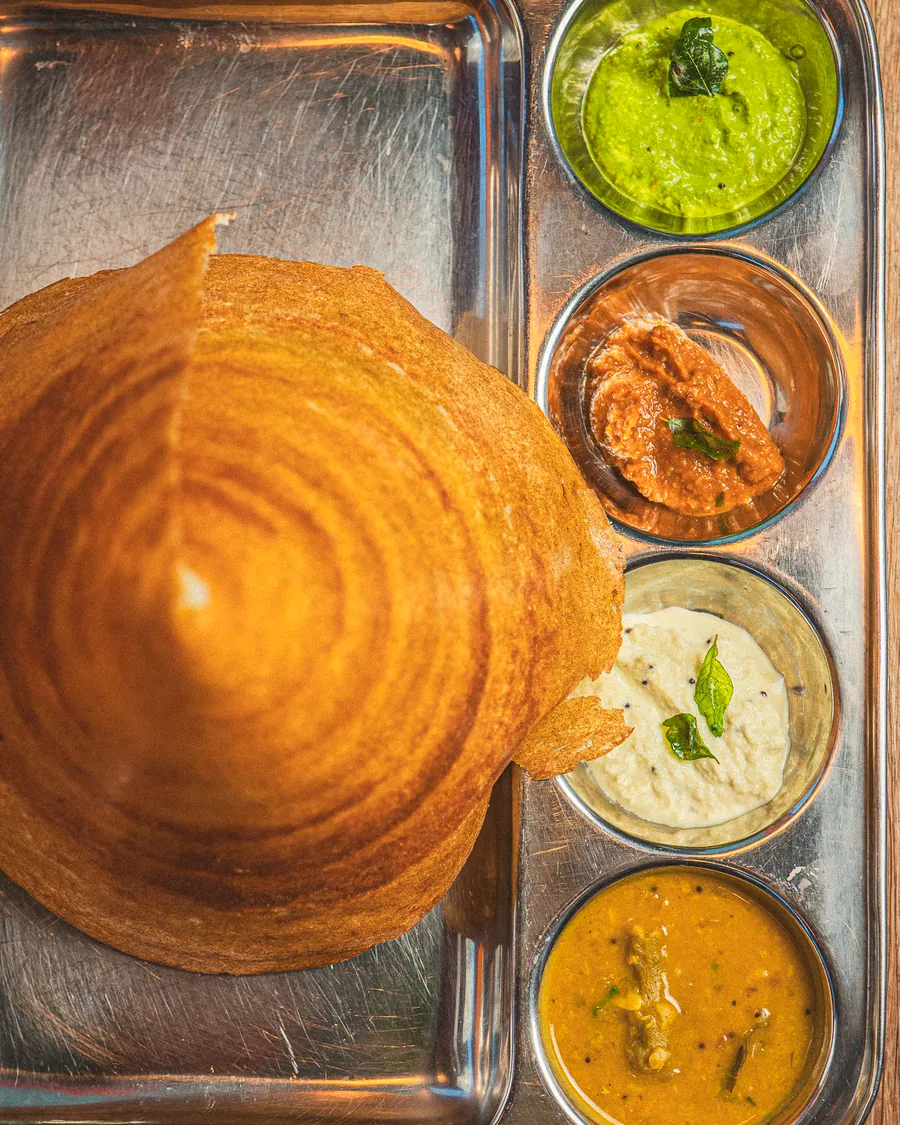 A tall cone of crisp dosa on a steel tray with four chutneys