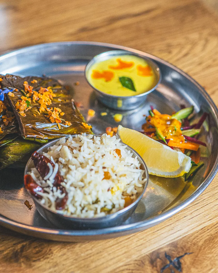 A round steel thali: rice, curry, a coconut sauce and lemon